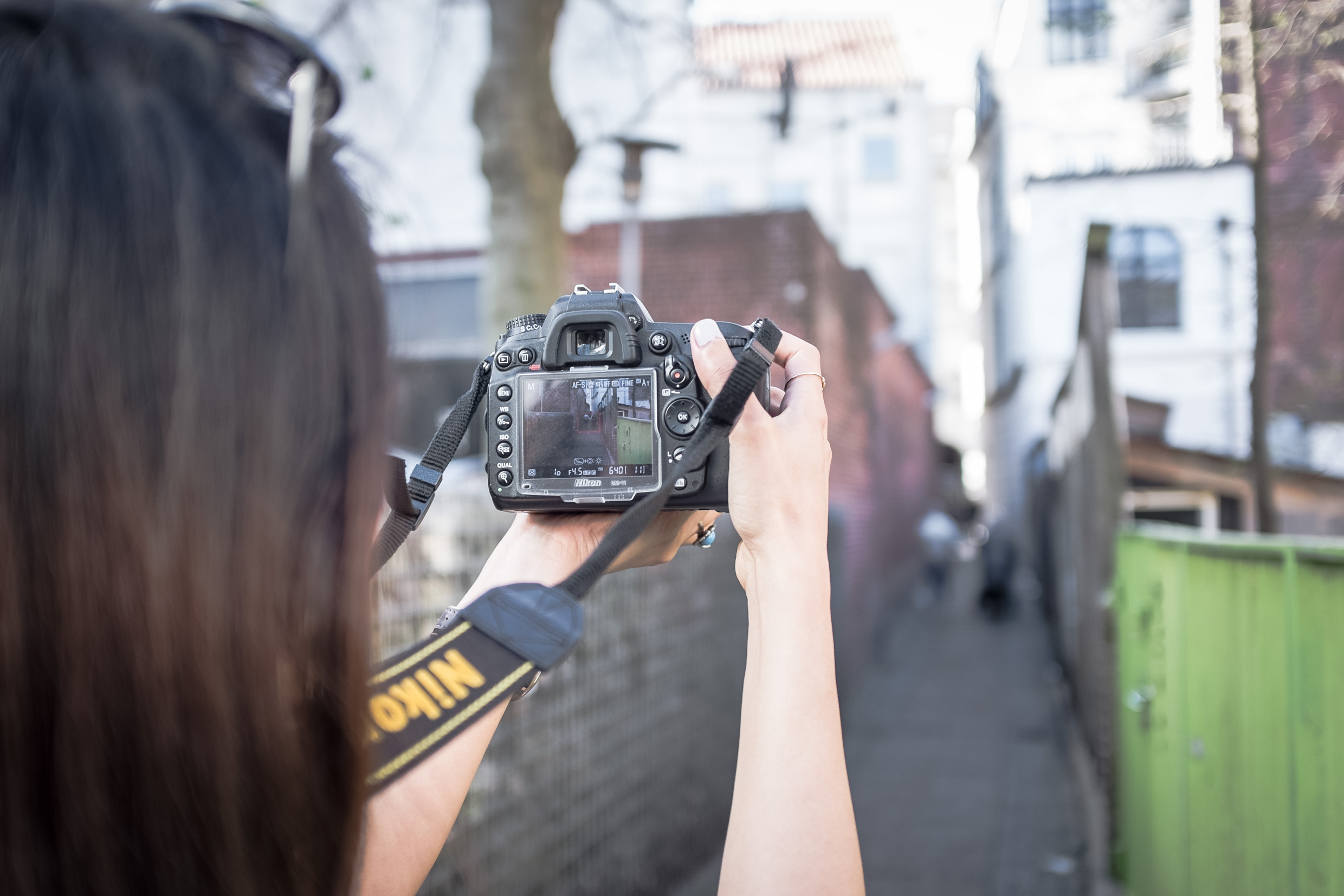 Arina holding a Nikon camera up in front of her, taking photos of an alley