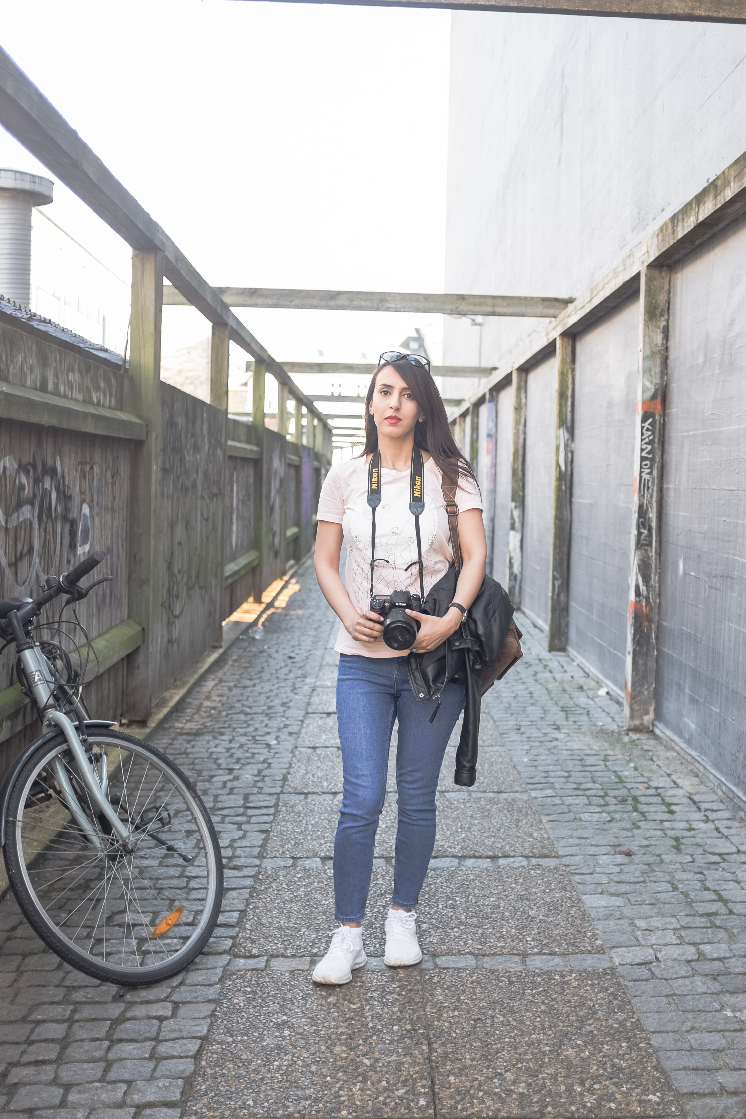 Arina standing with a Nikon camera in an alley with her bike next to her