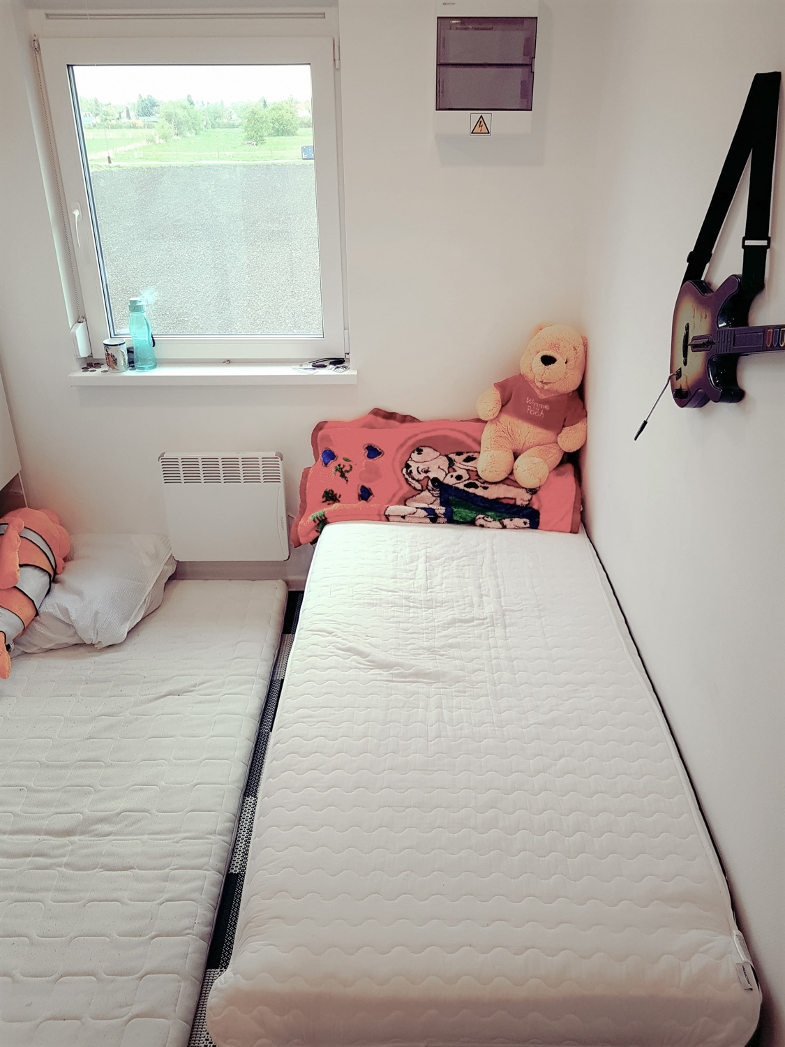 A room with a window, two mattresses and two teddy bears on it.