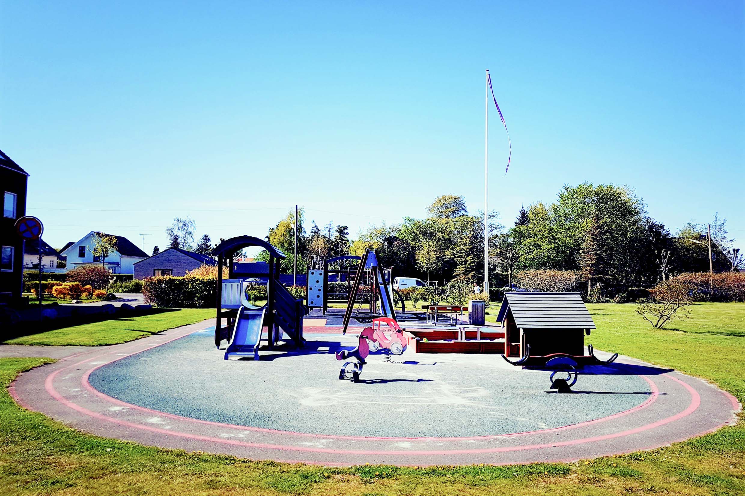 An outside playground with a slide, a small house, a sandbox, a swing and a bench.
