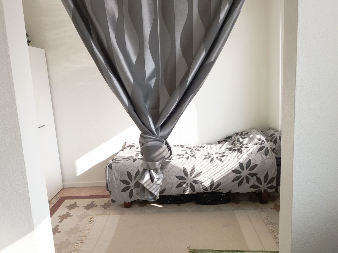 A bed behind a grey curtain with a knot on it
