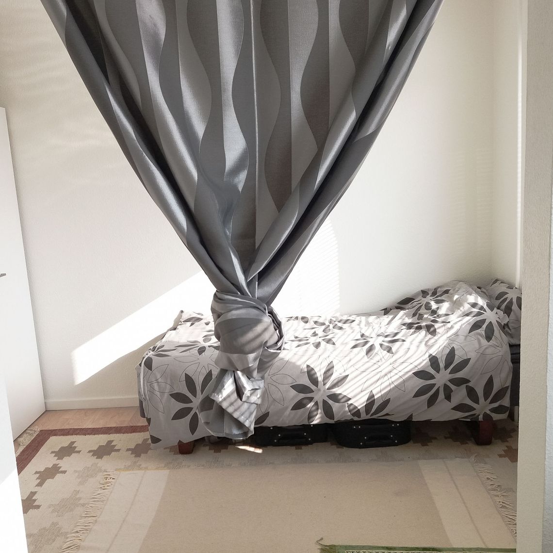 A bed behind a grey curtain with a knot on it