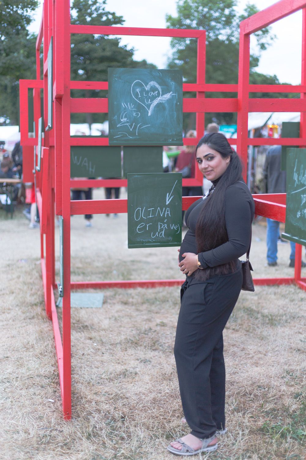 Hisham's wife standing with her hands on her pregnant belly in front of a sign saying "Olina is on her way out".