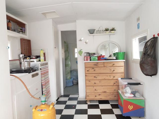 A kitchen with a black and white checkered floor, a yellow container, a wooden dresser with a lot of items on top of it.