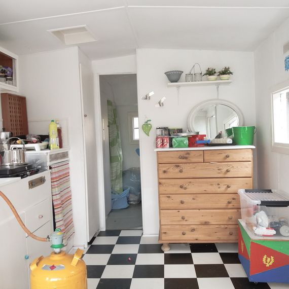 A kitchen with a black and white checkered floor, a yellow container, a wooden dresser with a lot of items on top of it.