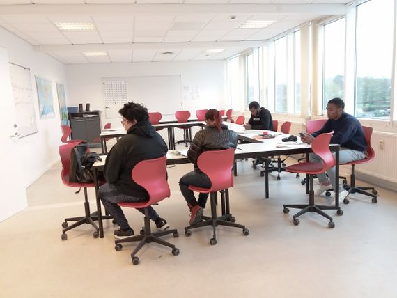 Four people sitting on red chairs in a classroom