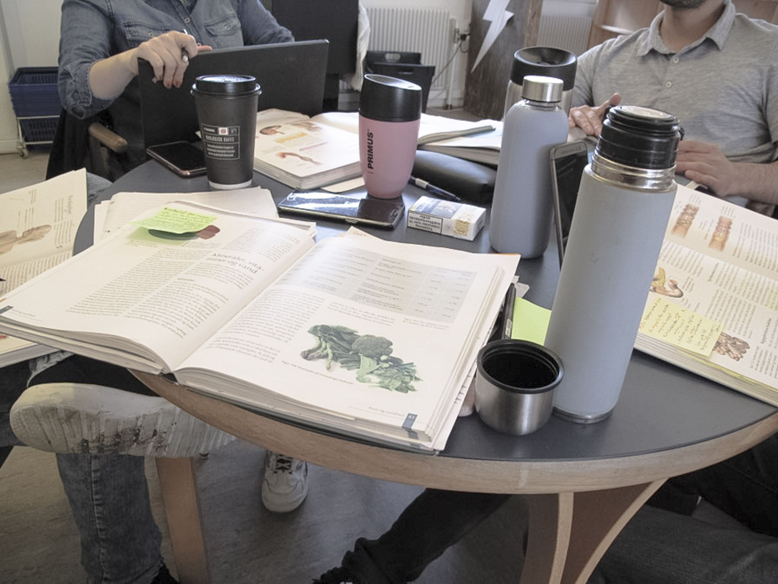 A table with open books placed on it and coffee cups.