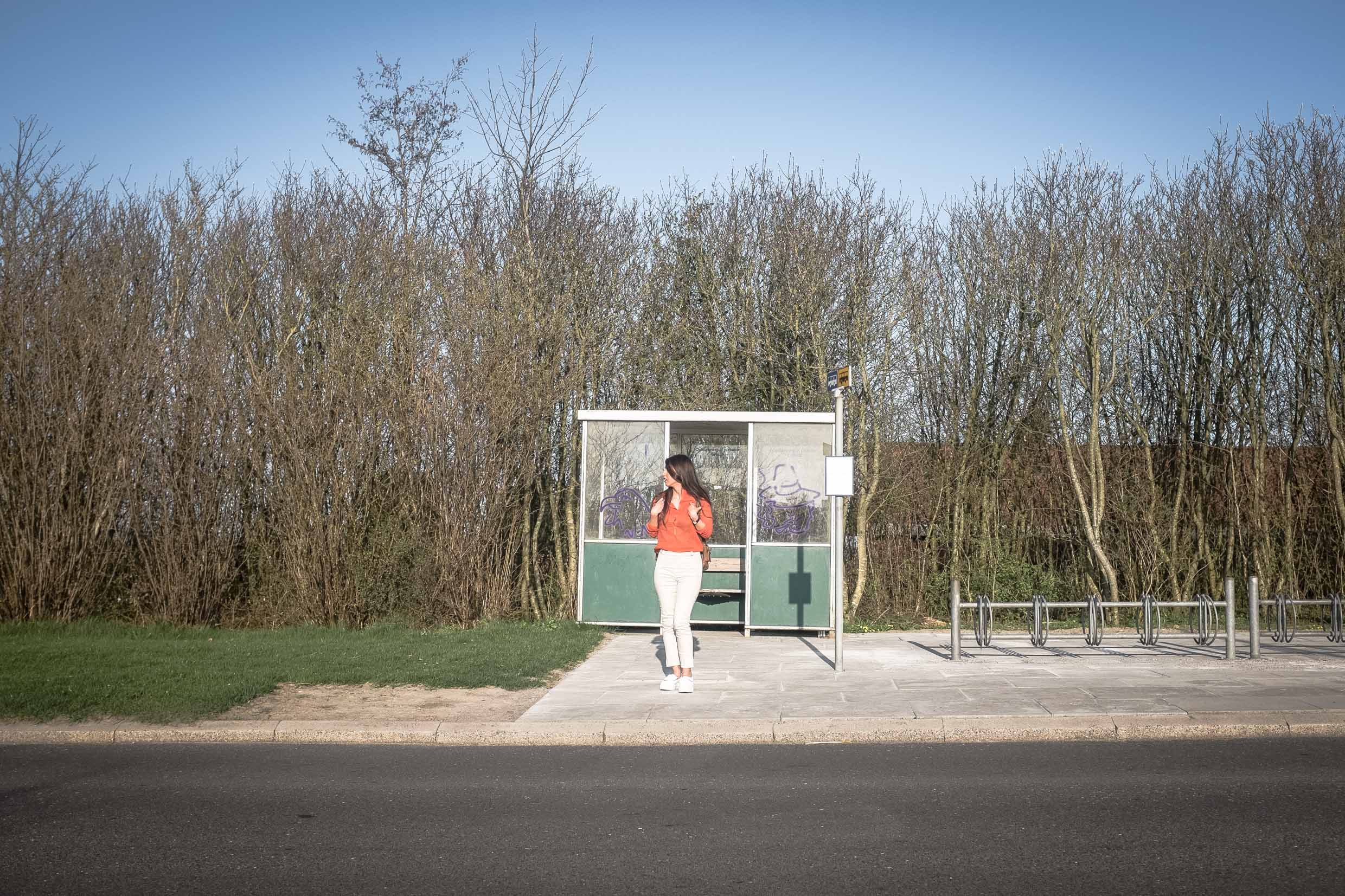 Arina standing in front of a bus stop with her backpack. 