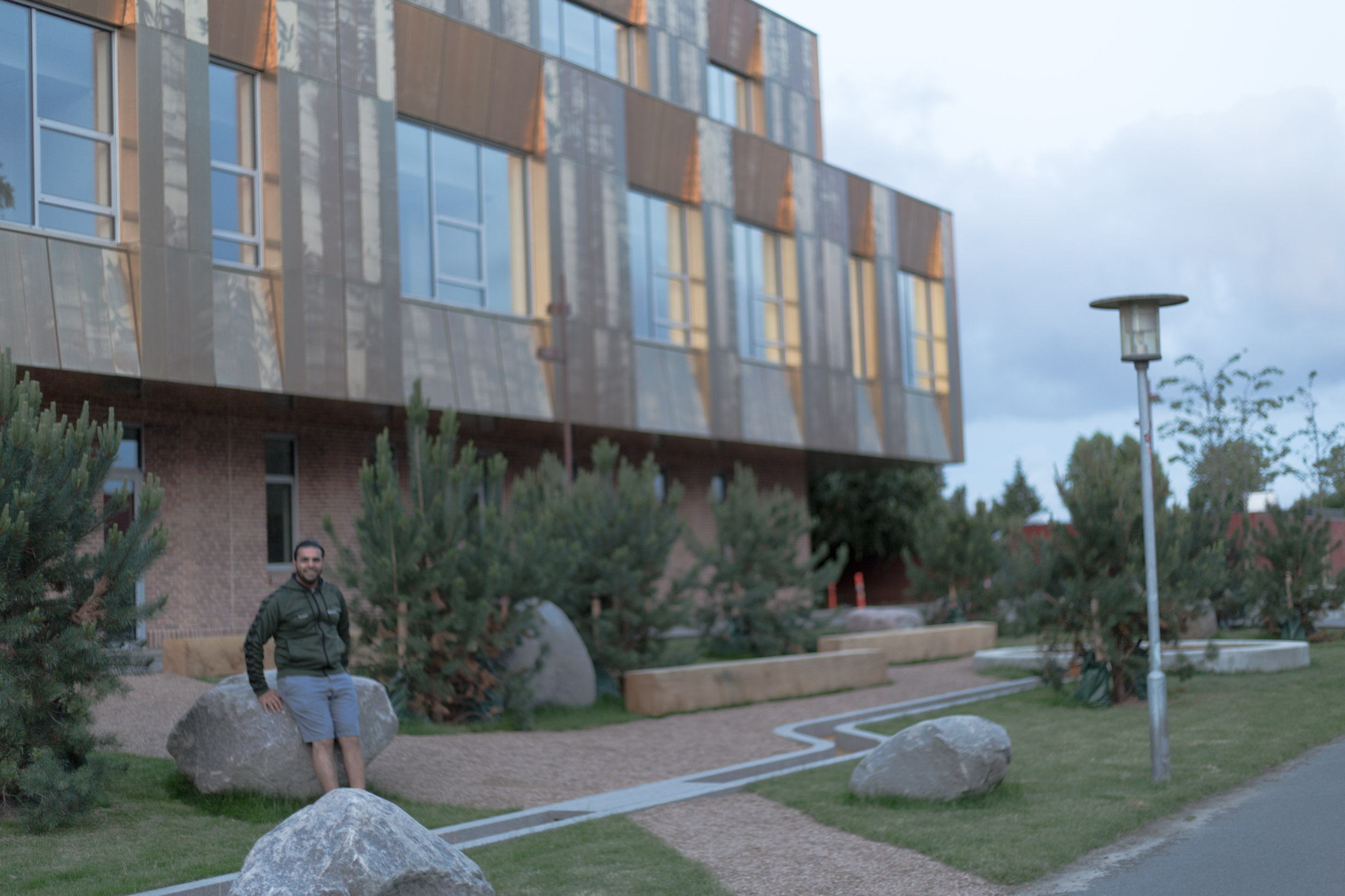 Hisham standing outside a building with a golden facade surrounded by trees and stones.