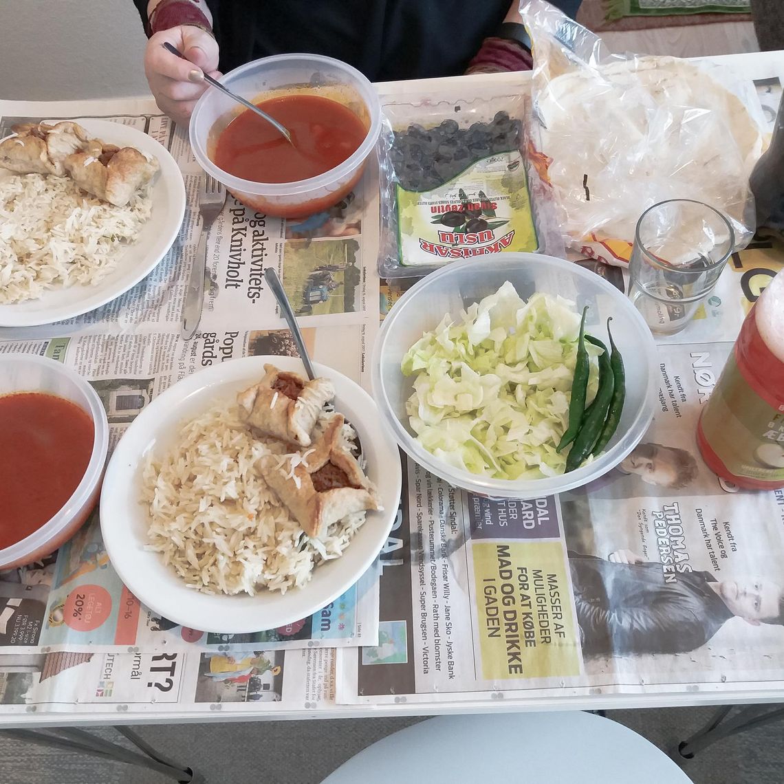 A table with a newspaper as table cloth and plates with rice, olives and a red soup on it