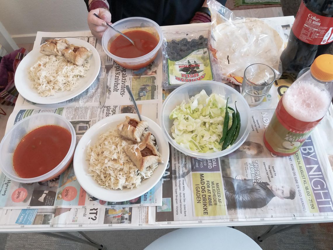 A table with a newspaper as table cloth and plates with rice, olives and a red soup on it