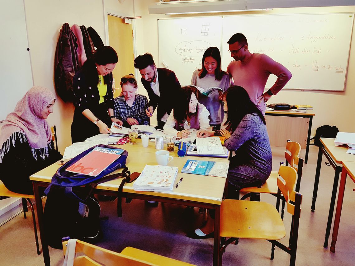 Eight people standing around a school table talking and looking at books.