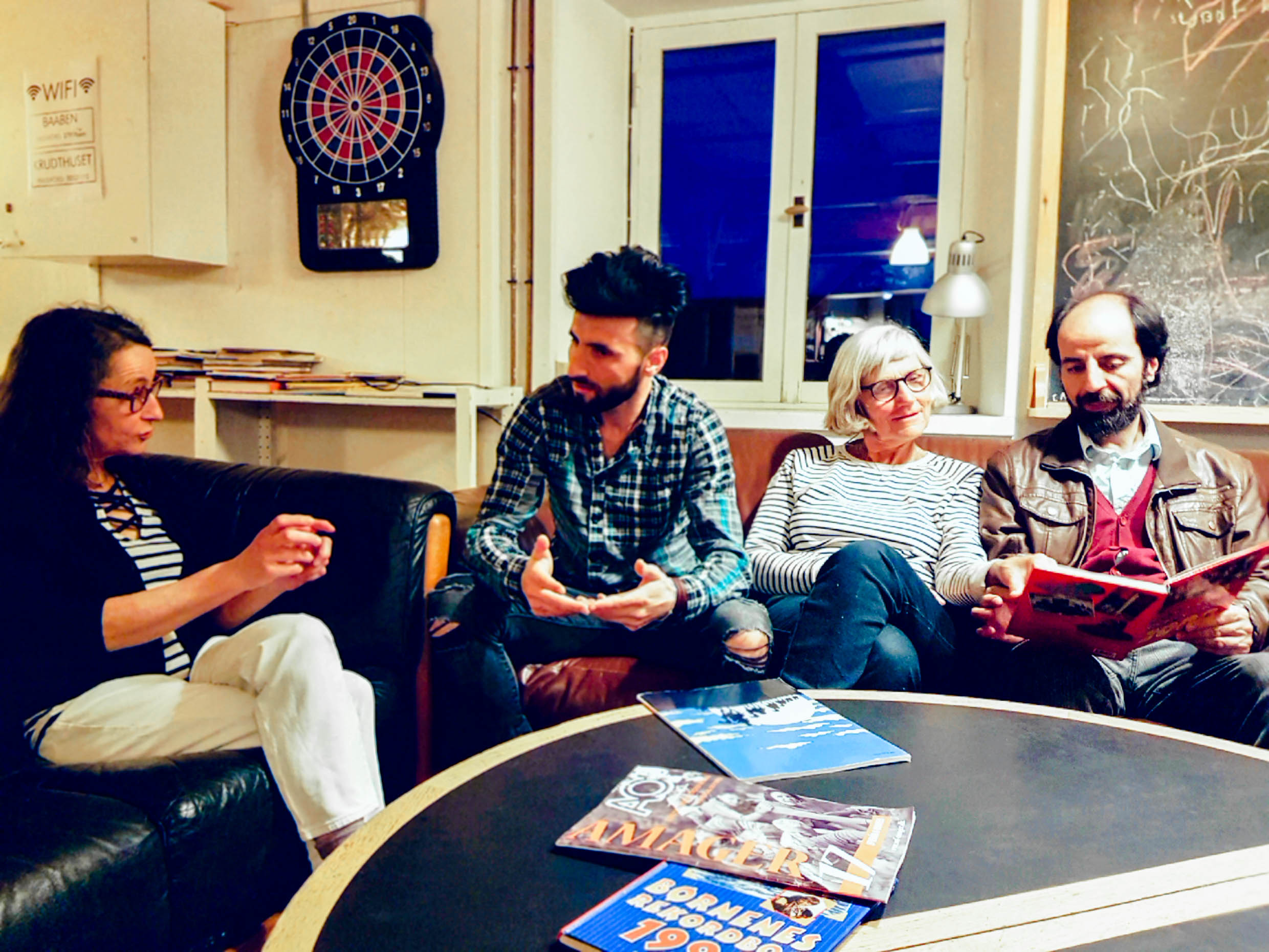 Rahim and three other persons sitting in two couches talking and looking in a book.