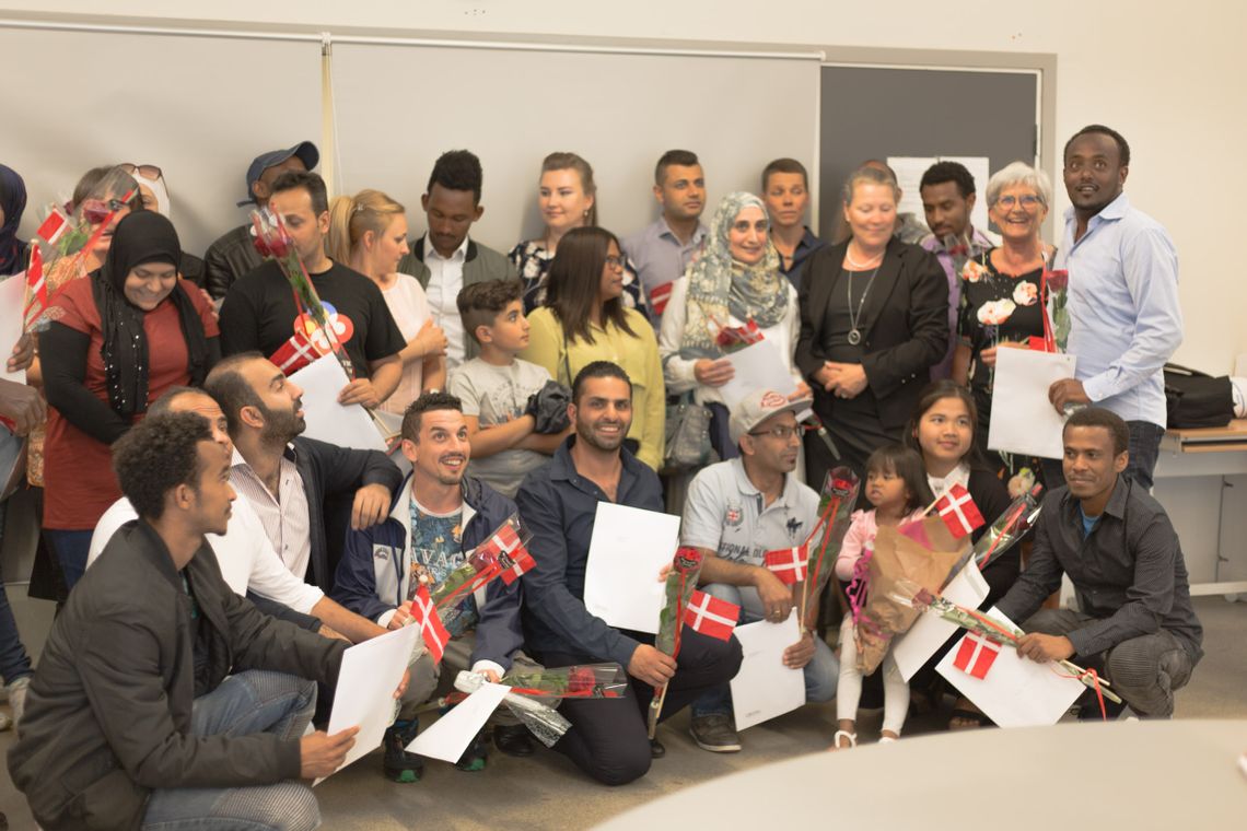 A large group of people with flowers, diplomas and Danish flags.
