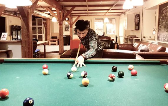 Rahim playing billiard i a room with brown couches and wooden poles.