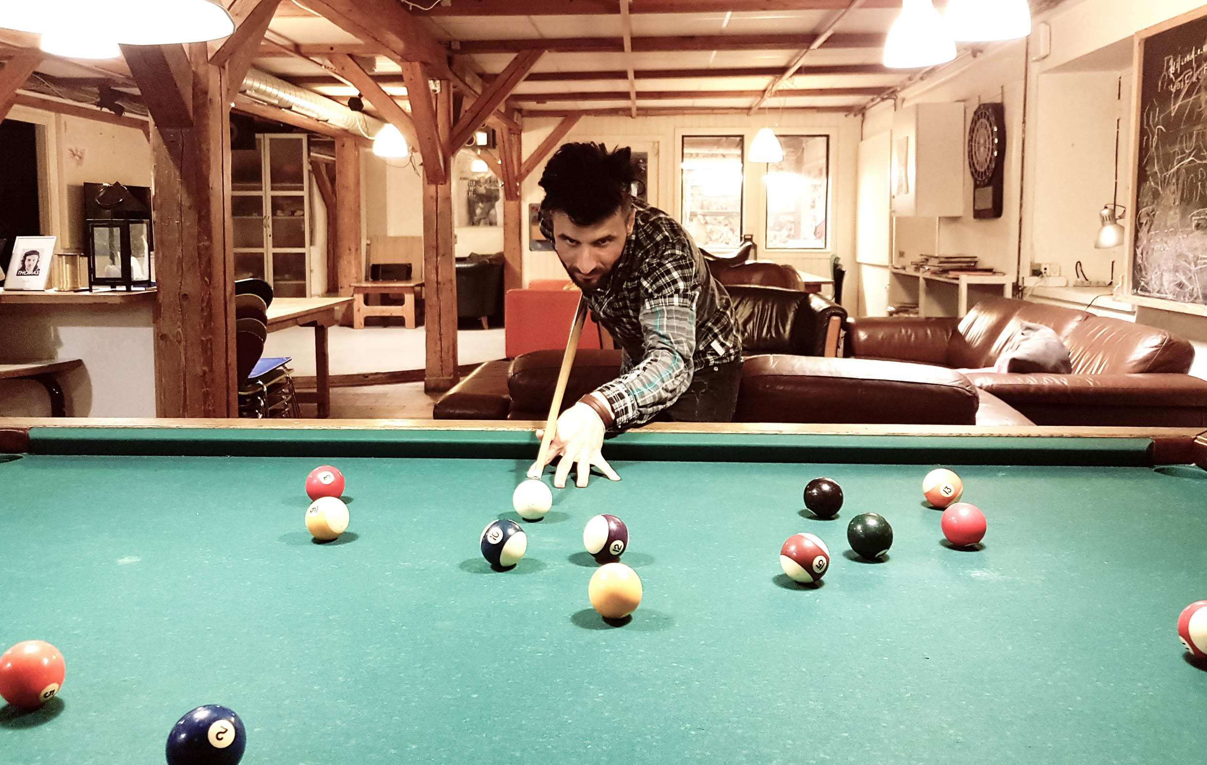 Rahim playing billiard i a room with brown couches and wooden poles.