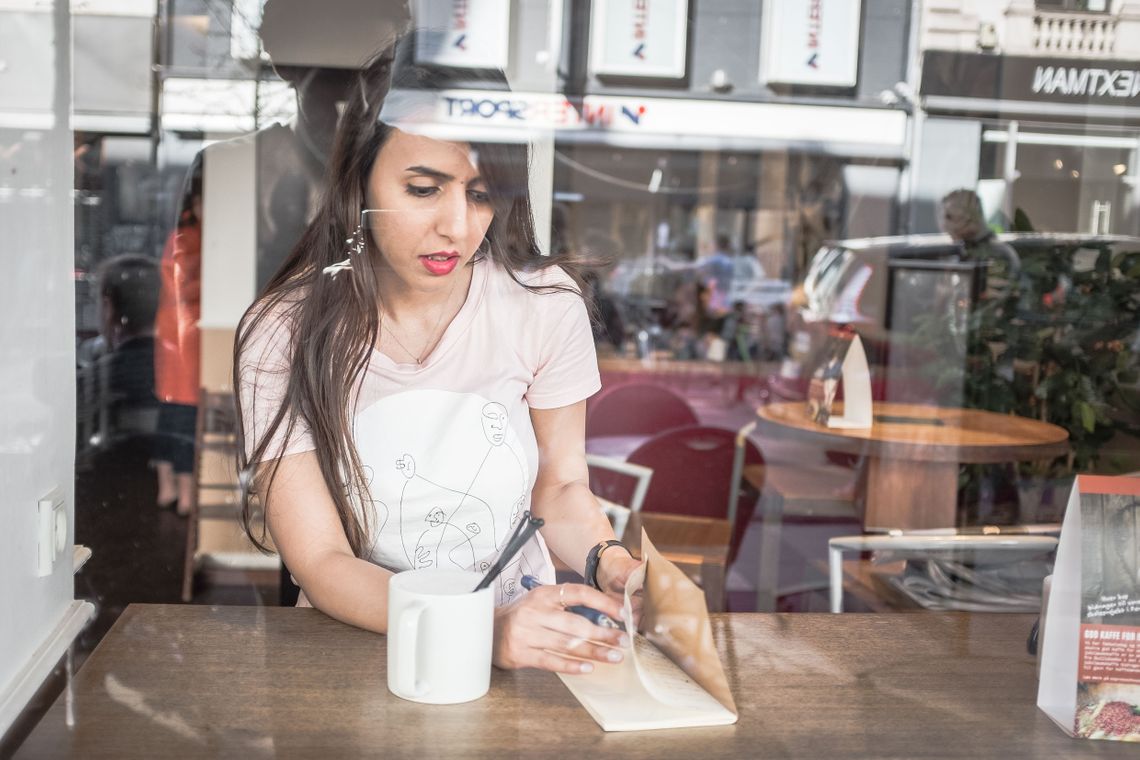 Arina sitting in a café with a cup and a book and a pencil