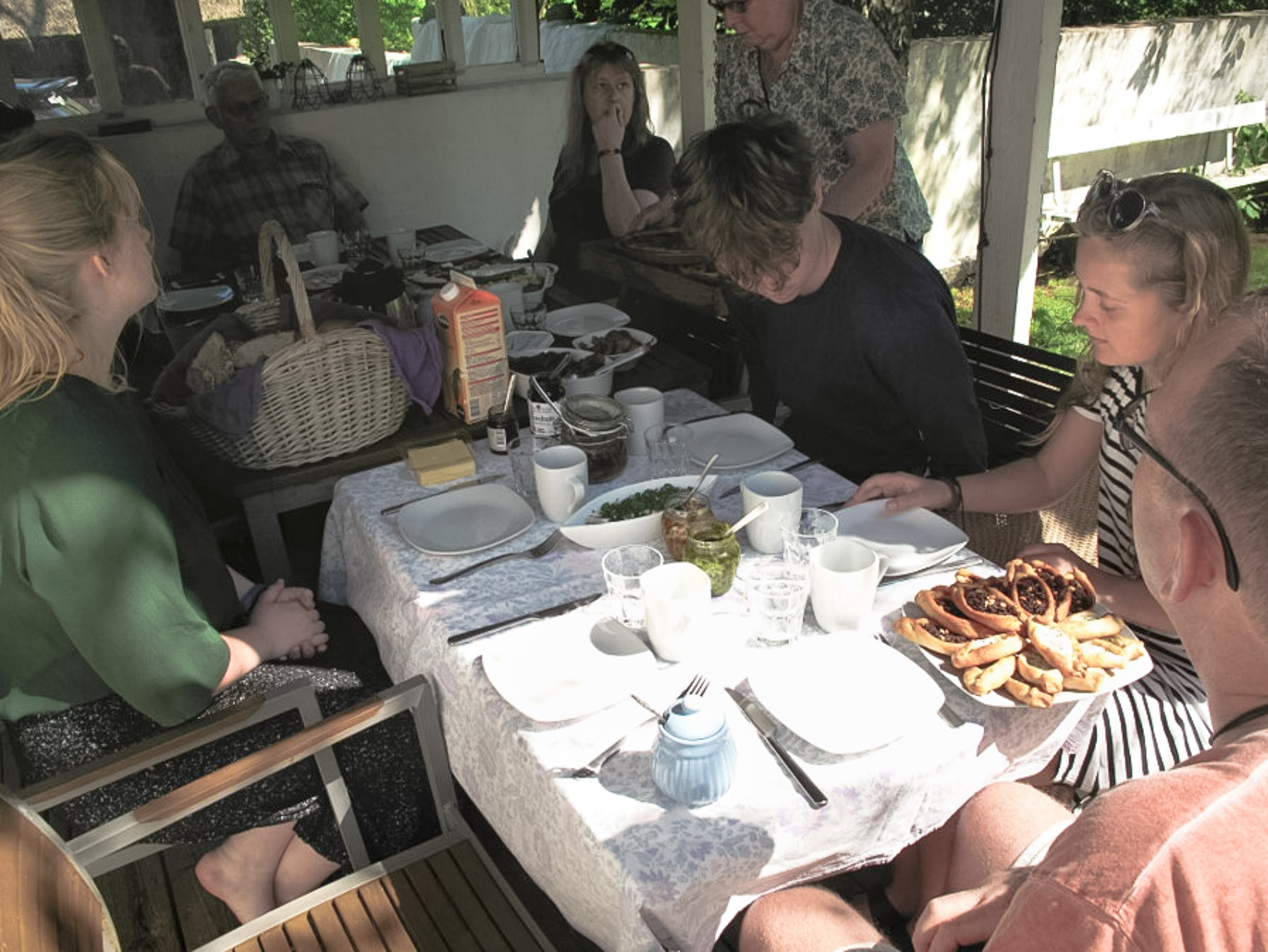 Six people witting around a table with plates and cakes.